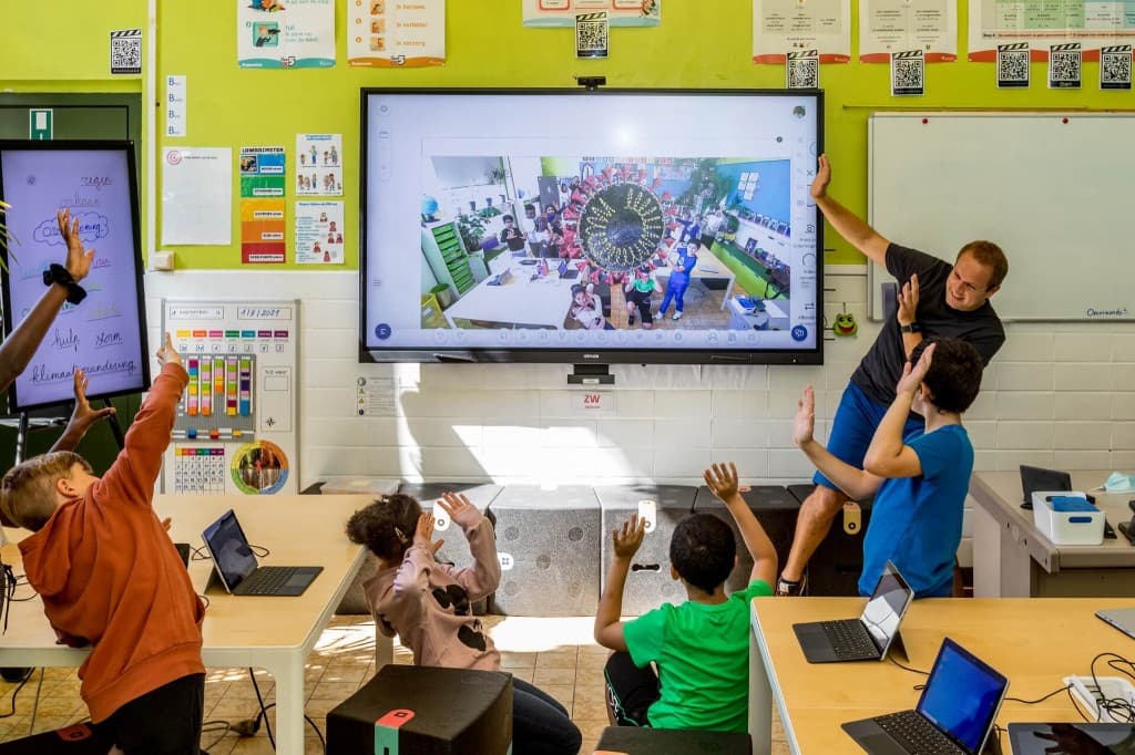 Kids and educator in a vibrant classroom with interactive screens and laptops